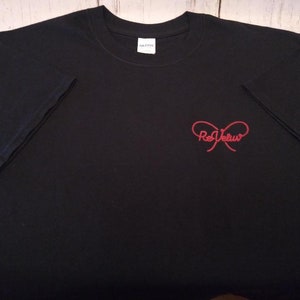 May include: A black short-sleeved t-shirt featuring a red graphic on the front right chest. The graphic consists of a stylized bow shape with the text ReVeluv written in a cursive font across the center of the bow. The shirt has a crew neckline.