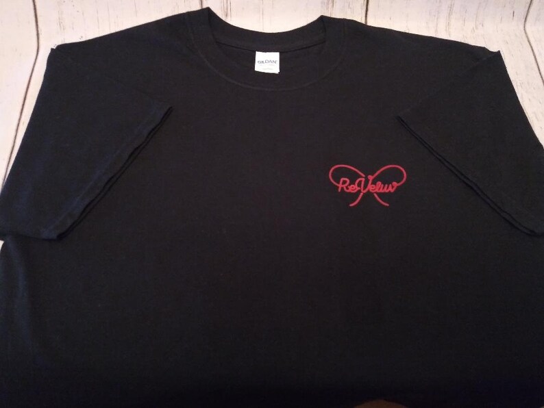 May include: A black short-sleeved t-shirt featuring a red graphic on the front right chest. The graphic consists of a stylized bow shape with the text ReVeluv written in a cursive font across the center of the bow. The shirt has a crew neckline.