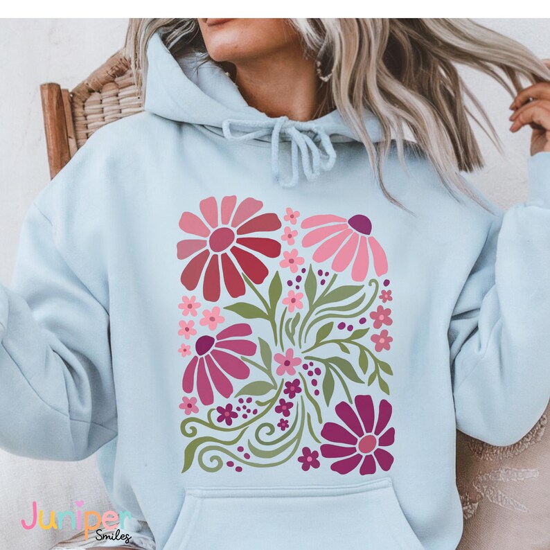 May include: Light blue hoodie featuring a floral design in shades of pink, red, and green. The graphic includes stylized flowers, leaves, and decorative swirls. The hoodie has a drawstring hood and a front pocket.