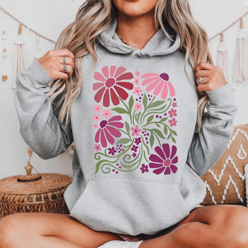 May include: A light gray hoodie featuring a floral design. The design includes large pink and magenta flowers, smaller pink flowers, green leaves, and a few purple berries. The hoodie has a front pocket and a drawstring hood.