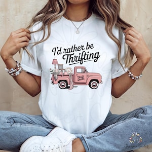 May include: White t-shirt featuring the text "I'd rather be Thrifting" in black script. A pink vintage truck graphic is filled with thrifted items. The truck has the words "Thrift Queen" on the side.