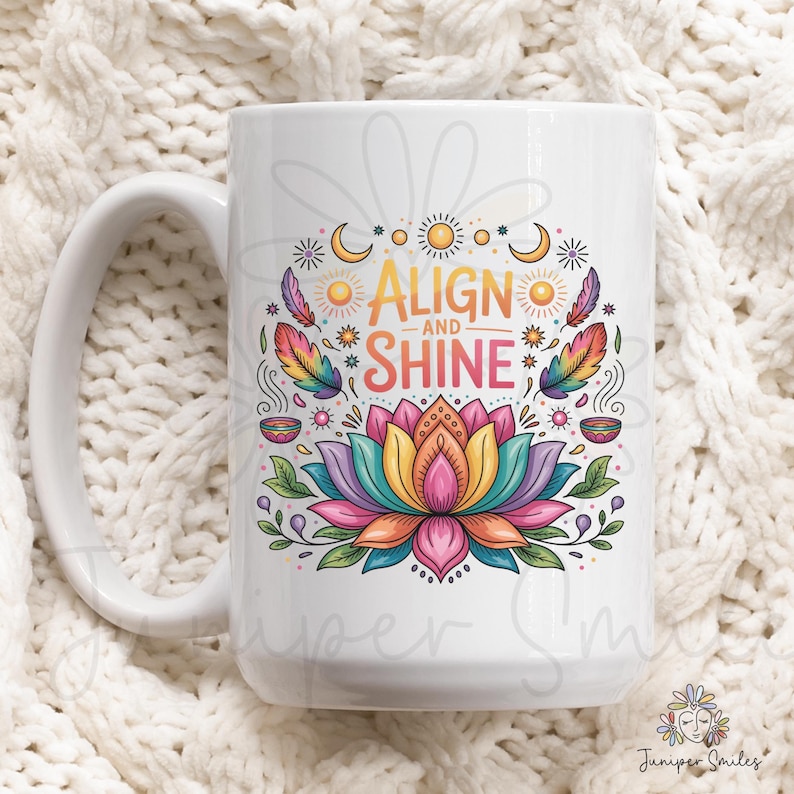 K&ouml;nnte beinhalten: Wei&szlig;er Keramikbecher mit gro&szlig;em Henkel, mit einem farbenfrohen Blumendesign mit den Worten "ALIGN and SHINE". Das Design umfasst eine Lotusblume, Federn, Sonnen und Monde. Der Becher hat eine gl&auml;nzende Oberfl&auml;che.