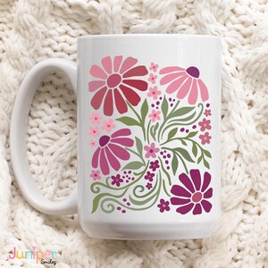 May include: White ceramic mug featuring a floral design in shades of pink and red with green leaves. The mug has a large handle and the text "Juniper Smiles" is visible at the bottom.