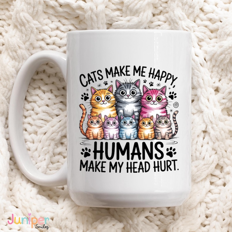 Puede incluir: Taza de cer&aacute;mica blanca con una ilustraci&oacute;n de siete gatos de dibujos animados de varios colores. La taza presenta el texto "CATS MAKE ME HAPPY, HUMANS MAKE MY HEAD HURT" en letras negras. La taza tiene un asa grande.