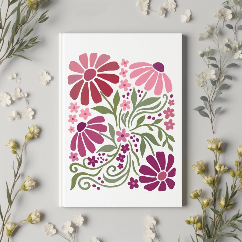 May include: A white notebook with a floral design. The design features stylized flowers in shades of pink and red, with green leaves and stems. The flowers are arranged in a symmetrical pattern.