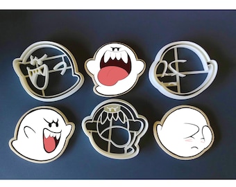 May include: Six white plastic cookie cutters shaped like ghosts from the video game Super Mario Bros. The cutters feature different expressions, including a ghost with a wide open mouth, a ghost with a tongue sticking out, and a ghost with its eyes closed.