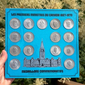 Peut inclure: Un panneau d'affichage carré bleu vif intitulé LES PREMIERS MINISTRES DU CANADA 1867-1970 présentant quatorze médaillons circulaires argentés avec des portraits de Premiers ministres canadiens et une illustration du Parlement au centre.