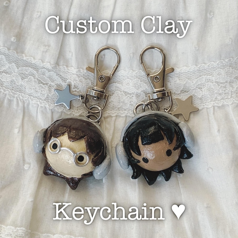 May include: Two custom clay keychains featuring cartoon character designs. One has brown hair and glasses, the other has black hair. Each keychain has a silver clasp and a star charm. The text "Custom Clay Keychain" is displayed.