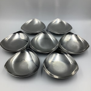 Może przedstawiać: Zestaw siedmiu srebrnych, trójkątnych talerzy do serwowania. Talerze są ułożone w okrągły wzór na białym tle.