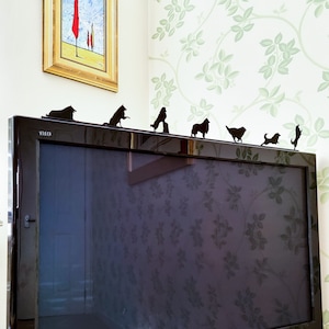 Op de afbeelding: Een zwarte flatscreen televisie met het woord "VIERA" aan de voorkant. De televisie staat op een tafel met een witte muur erachter. Er zijn zwarte silhouetten van honden op de bovenkant van de televisie.