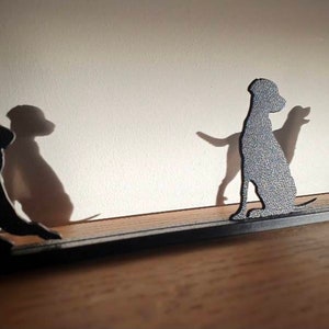 May include: A metal silhouette of four dogs standing on a black metal bar. The dogs are all facing the same direction, and their shadows are cast on the wall behind them.