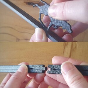May include: Close-up of a black metal frame with a decorative cutout of a dog. The frame is being assembled by two hands.