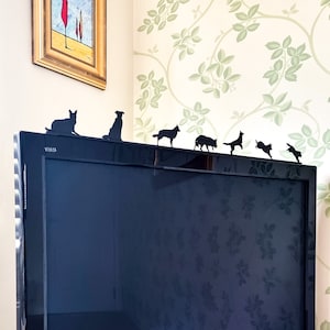 May include: A black television with a silver trim sits on a shelf.  Silhouettes of dogs are placed on top of the television, creating a playful and whimsical scene.