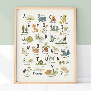 May include: A framed print featuring an illustrated alphabet with camping and outdoor themes. Each letter is paired with a corresponding word and image, such as "A" for adventure, a campfire, a dog, and a tent. The artwork has a vintage, hand-drawn style.