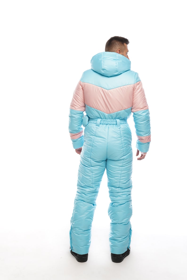 Op de afbeelding: Een lichtblauw skibroek met een roze paneel op de rug. Het pak heeft een capuchon en een ritssluiting.