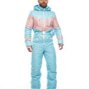 Op de afbeelding: Een lichtblauw en roze skipak met een capuchon en een riem. Het pak is gemaakt van een gewatteerd materiaal en heeft een ritssluiting.