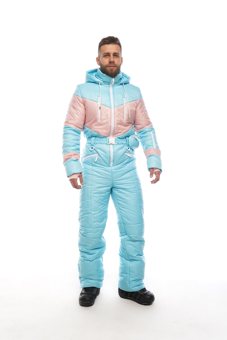 Op de afbeelding: Een lichtblauw en roze skipak met een capuchon en een riem. Het pak is gemaakt van een gewatteerd materiaal en heeft een ritssluiting.