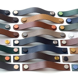 Peut inclure: Une collection de poignées de meubles décoratives de différentes couleurs et motifs. Les poignées sont en cuir et en métal, avec un design incurvé. Les couleurs incluent le noir, le marron, le bleu, le vert et le blanc. Les accents métalliques sont argentés, dorés et cuivrés.