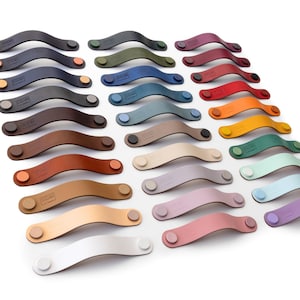 Puede incluir: Una variedad de 20 tiradores de armario de cuero en diferentes colores, incluyendo blanco, beige, marrón, rojo, naranja, amarillo, verde, azul, morado y gris. Los tiradores están dispuestos en un patrón escalonado sobre un fondo blanco.