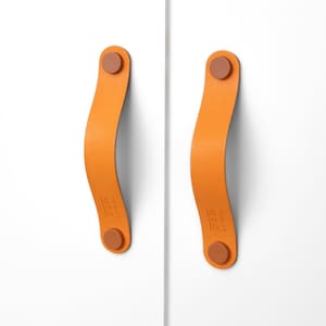 May include: Two orange leather cabinet pulls with brown metal accents. The pulls are attached to a white surface.