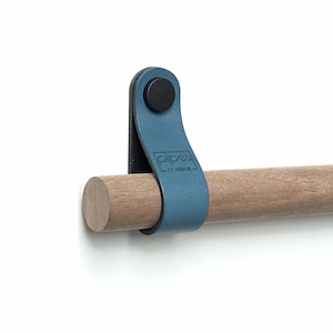 Può includere: Un cinturino in pelle blu con un bottone nero e il testo "oprea" è attaccato a un'asta di legno.