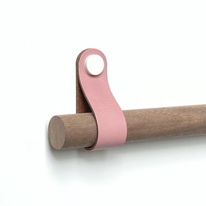 Può includere: Un'asta di legno con un cinturino in pelle rosa e un bottone bianco. Il cinturino ha il testo "DIXX" su di esso.