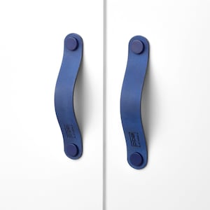 Op de afbeelding: Twee blauwe leren kastgrepen met een afgeronde vorm en een kleine blauwe knop aan elk uiteinde. De grepen hebben het woord "RECO" erop gedrukt.