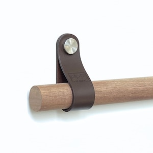 Può includere: Un cinturino in pelle marrone con un fermaglio in metallo argentato è attaccato a un tassello di legno. Il cinturino riporta il testo "piper - the modern". Il tassello di legno è di colore marrone chiaro.