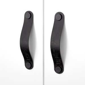 May include: Two black leather cabinet pulls with a curved design and round metal ends.