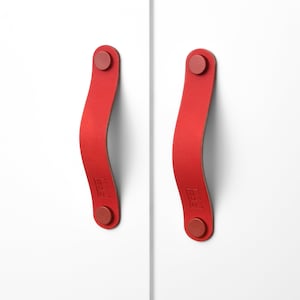 Peut inclure: Deux poignées de porte en cuir rouge avec une forme incurvée et un bouton rond à chaque extrémité.