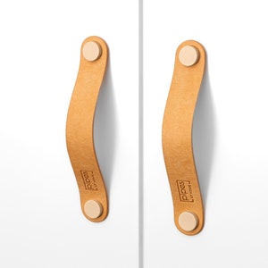 Puede incluir: Dos tiradores de armario de cuero marrón con pomos redondos blancos. Los tiradores tienen la palabra "PIPES" impresa.