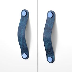 May include: Two blue leather cabinet pulls with silver metal accents. The pulls are curved and have a distressed look.