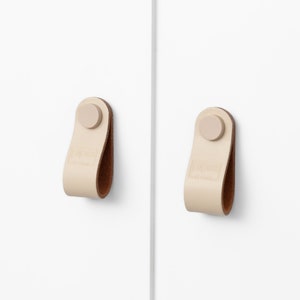 May include: Two off-white leather cabinet pulls with a brown leather loop and a beige round knob.