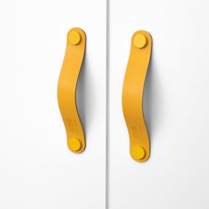 May include: Two yellow leather cabinet pulls with yellow round knobs. The pulls are curved and have a subtle texture.