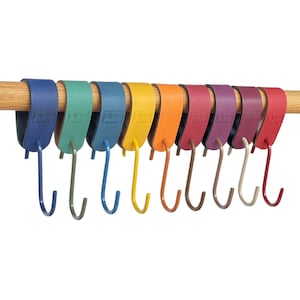 Könnte beinhalten: Eine Reihe farbiger Haken, die an einer Holzstange hängen. Die Haken sind in Regenbogenfarben gehalten, darunter Blau, Grün, Gelb, Orange, Rot und Lila. Jeder Haken ist an einem Lederriemen befestigt.