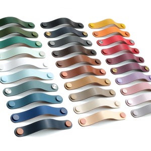 May include: A collection of arched cabinet handles arranged in three columns, featuring a variety of solid colors including green, blue, red, yellow, brown, and neutral tones. Each handle is secured at both ends with circular metal fasteners.