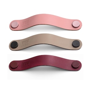 May include: Three leather drawer pulls in pink, beige, and burgundy. Each pull has a round metal knob on each end.