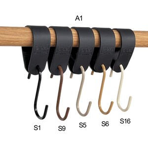 May include: A row of six black leather-like hangers with metal hooks, attached to a wooden rod. The hooks are in various colors: black, brown, beige, and off-white. The text "A1", "S1", "S9", "S5", "S6", and "S16" are visible.