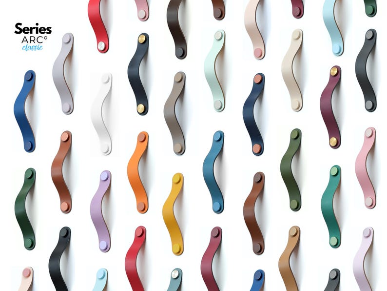 May include: A collection of Series ARC classic cabinet handles in various solid colors, including red, blue, yellow, green, black, white, and pastel shades. Each curved handle features two circular mounting points with metallic fasteners.