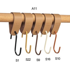 May include: Six leather-look hooks in various colors, including black, gold, brown, cream, and rust, are attached to a wooden rod. Each hook is labeled with a letter and number combination. The text "A11" is visible.