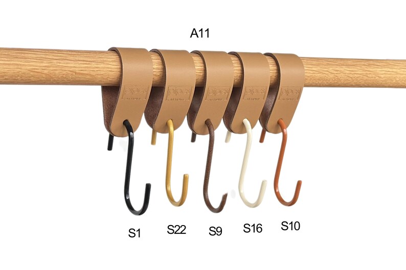 May include: Six leather-look hooks in various colors, including black, gold, brown, cream, and rust, are attached to a wooden rod. Each hook is labeled with a letter and number combination. The text "A11" is visible.