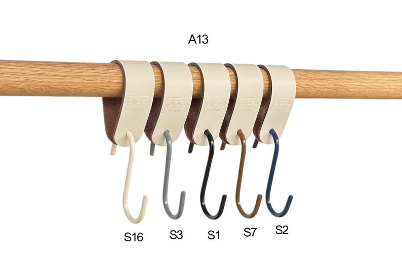 May include: A row of six S-shaped hooks in various colors, suspended from a wooden rod. The hooks are cream, gray, black, brown, and navy blue. The hooks are attached to cream-colored leather straps.