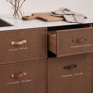 May include: Dark wood kitchen cabinetry featuring leather drawer pulls in various colors. Labels include A13 Camel | M2 Gold, A6 Hazelnut | C14 Choco, A7 Terracotta | M3 Copper, and A5 Espresso | C13 Coffe. One drawer is partially open, revealing the interior.