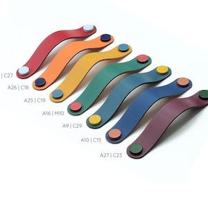 May include: Seven curved leather drawer pulls in red, orange, yellow, green, teal, blue, and purple, each secured by two contrasting circular fasteners. Text labels A29 | C27, A26 | C18, A25 | C19, A16 | M10, A9 | C29, A10 | C15, and A27 | C23 are visible.