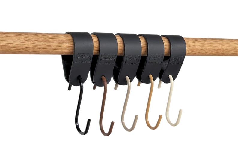 May include: A set of six black metal S-hooks hanging from a wooden rod. The hooks are in varying colors: black, brown, beige, and off-white. The hooks are designed to hang items.