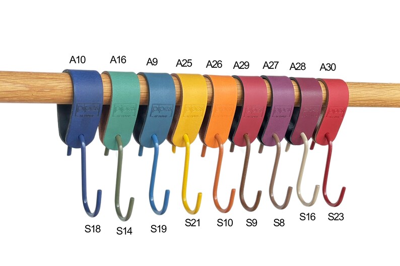May include: A collection of colorful, leather-wrapped hooks hanging from a wooden rod. The hooks are in various colors, including blue, green, yellow, orange, red, and purple. Each hook has a metal hook attached. The hooks are labeled with letters and numbers.