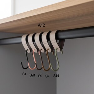 May include: A set of six S-shaped hooks in various colors, hanging from a black rod. The hooks are black, pink, brown, and green. The hooks are labeled S1, S24, S9, S7, and S14. The hooks are hanging under a wooden shelf.