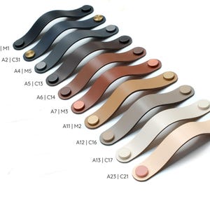 May include: A collection of curved cabinet handles in various colors including black, brown, tan, beige, and cream. Each handle features two circular metal or matching colored fasteners at the ends. Labels A1|M1, A2|C31, A4|M5, A5|C13, A6|C14, A7|M3, A11|M2, A12|C16, A13|C17, and A23|C21 are printed next to each corresponding handle.