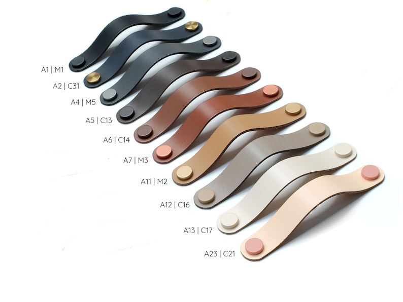 May include: A collection of curved cabinet handles in various colors including black, brown, tan, beige, and cream. Each handle features two circular metal or matching colored fasteners at the ends. Labels A1|M1, A2|C31, A4|M5, A5|C13, A6|C14, A7|M3, A11|M2, A12|C16, A13|C17, and A23|C21 are printed next to each corresponding handle.