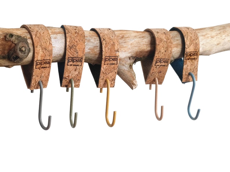 Pu&ograve; includere: Cinque ganci avvolti in sughero con ganci in metallo di diversi colori: grigio, verde, giallo, rosa e blu. I ganci sono attaccati a un ramo di legno.